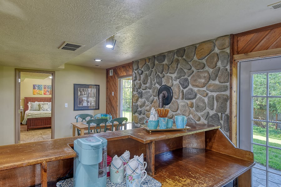 Chic turquoise coffee station on a restored vintage bar invites morning rituals, flowing past the textured rock wall and dining area into a tranquil bedroom with a luxuriously inviting queen bed.