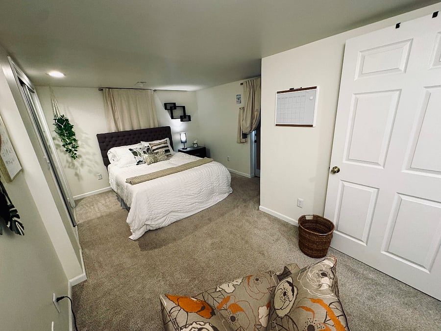 Garden Bedroom (photo 1) with nightstand, closet, hangers, desk, comfy chair and dresser. Interior closet organizer with shelving. Additional closet space (that houses the adjustable standing desk). Emergency exit door. Mirrored closet doors. Queen bed. Blackout curtains.