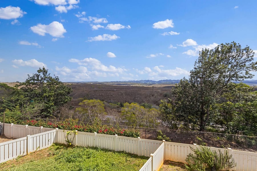 Behind the white picket fence, a masterpiece awaits: undulating terrain, vibrant foliage, and mountains in the distance. This breathtaking view brings tranquility to every moment.