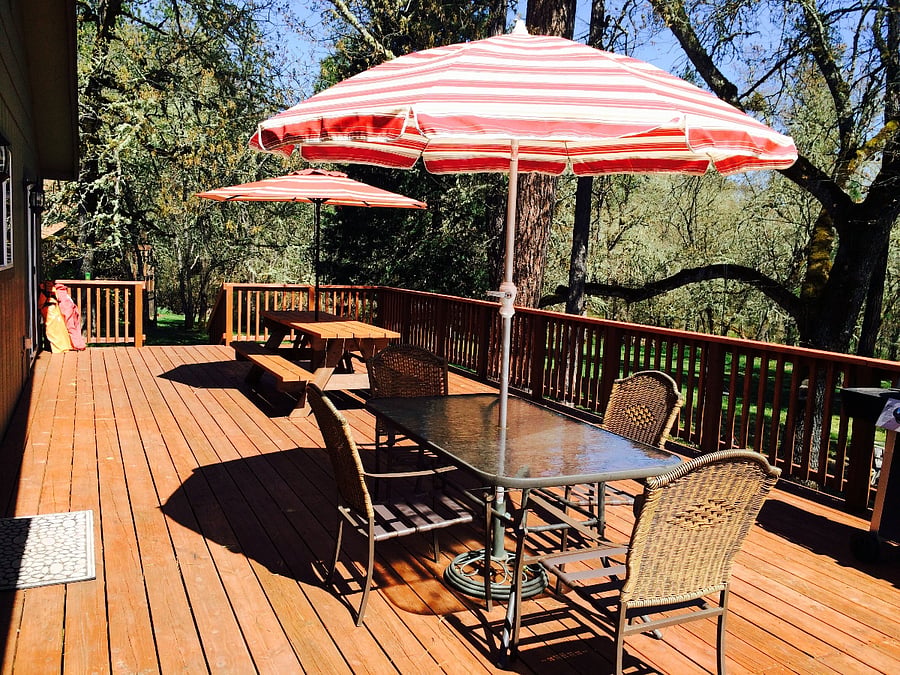 Large deck with gas BBQ, two seating areas with covered umbrellas, and views of the river.