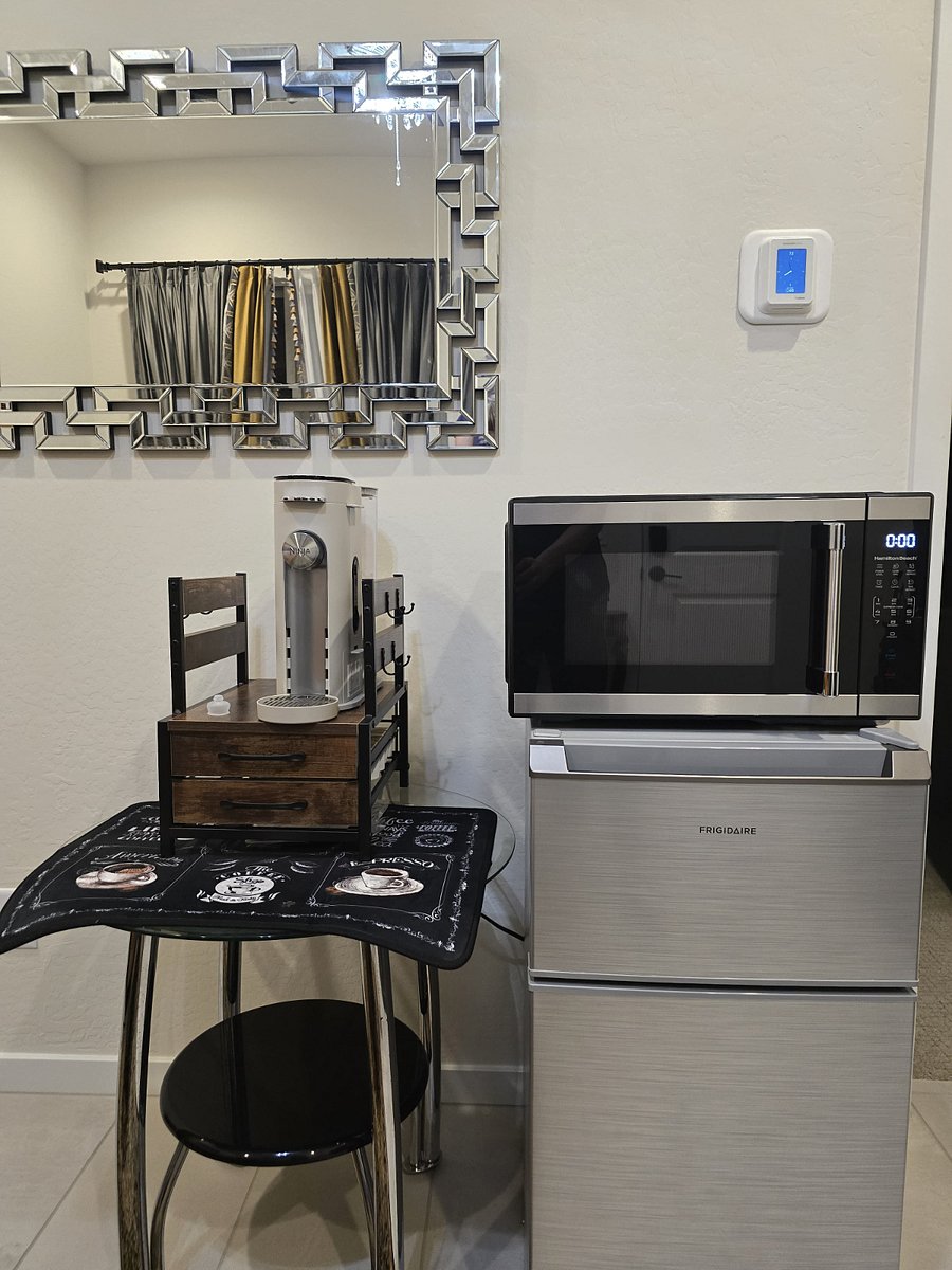 Room A Coffee Station
Guests enjoy a sleek, high-end coffee setup featuring a premium machine that brews hot, cold, and froths milk with ease. The unit sits on a modern glass table with neatly organized pods and accessories below. A microwave above adds extra convenience, while a decorative sign and geometric mirror nearby bring personality and polish to the space.