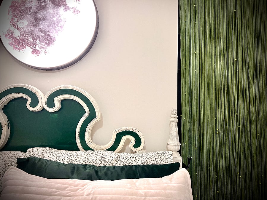The Moon Room - Detail
This a close-up of the bedding, the headboard, the Lunar Reading Light and the large walk-in closet of the Moon Room (behind the green fringe doorway). The closet has plenty of hangers and a chest of drawers. The moon is remote control operated and change colors and brightness.
You'll notice the bed is very lush and is meant to promote deep sleep. The room is near blackout with the blinds pulled shut, the ceiling fan offers a breeze, and the sheets and velvet coverlet are a pleasure to sleep in. The mattress itself is a work of art and is soft and delicious. We hope you love it.