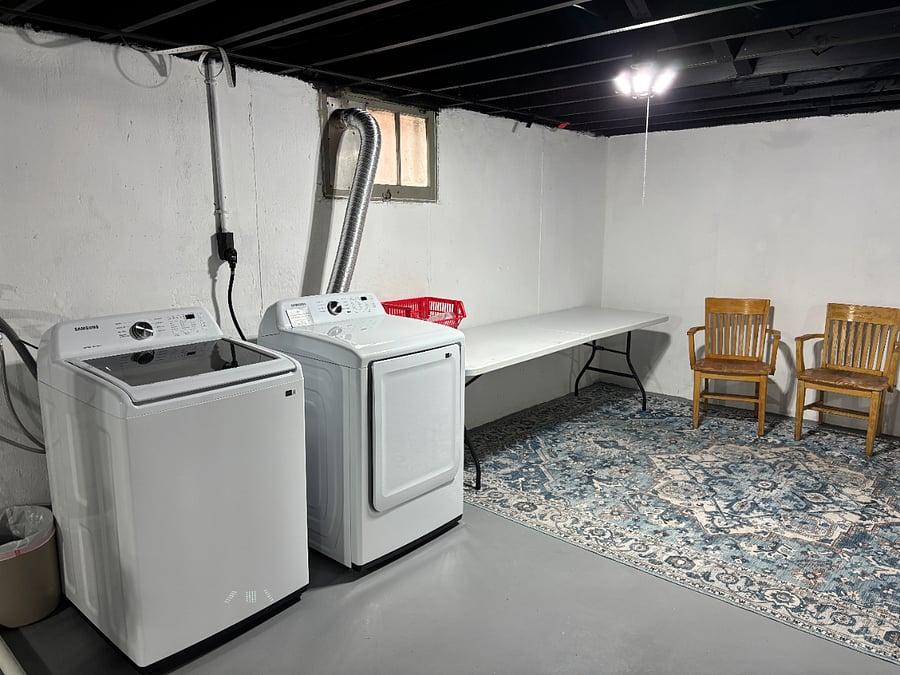 Basement with washer/dryer combo, folding area and chairs. 