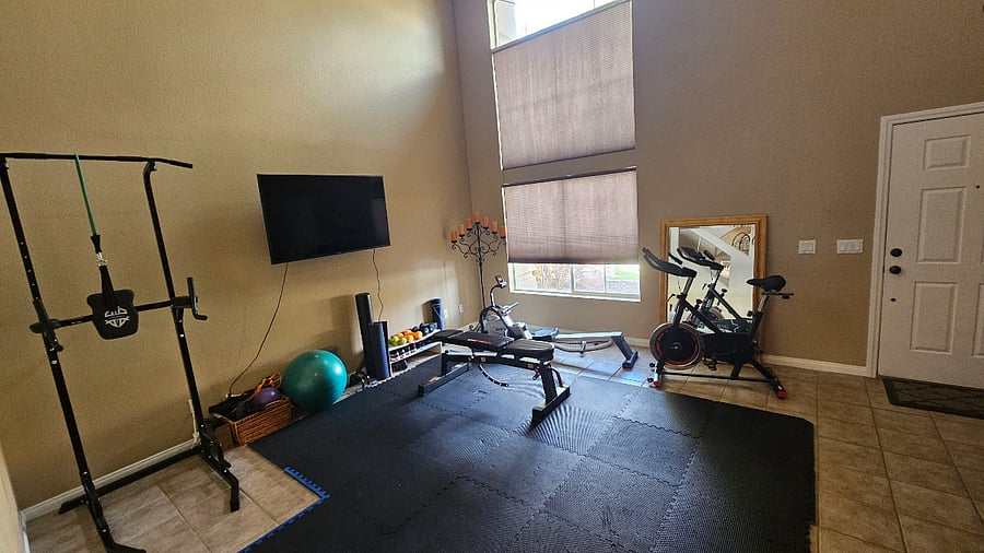 Home gym with smart TV, indoor bike, rowing machine, rack, small weights, bench, yoga blocks, ball and bands.