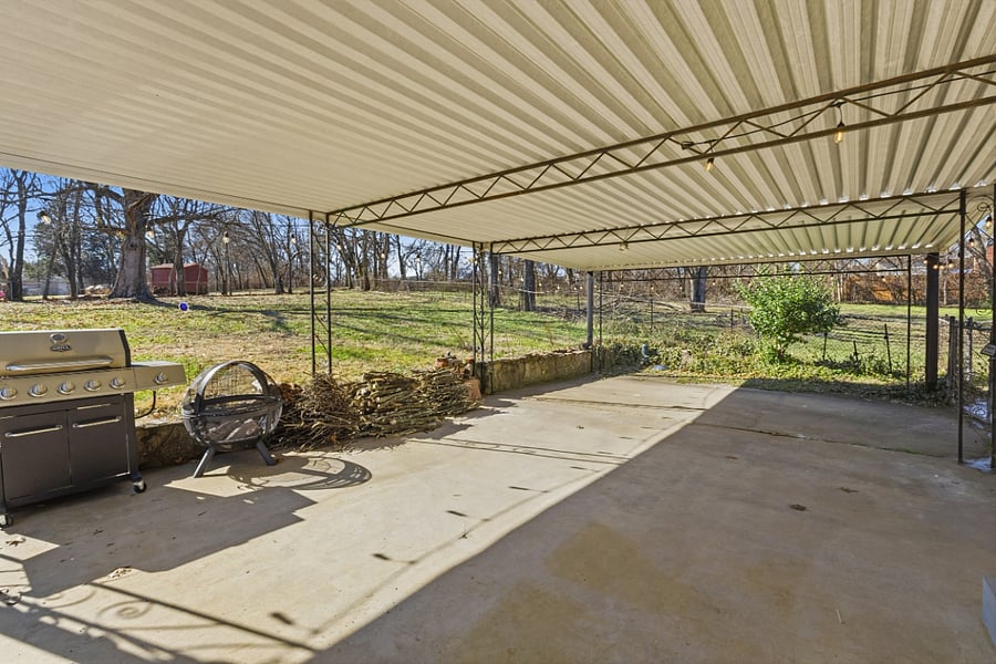 Carport features propane grill, portable firepit, views of the back yard.