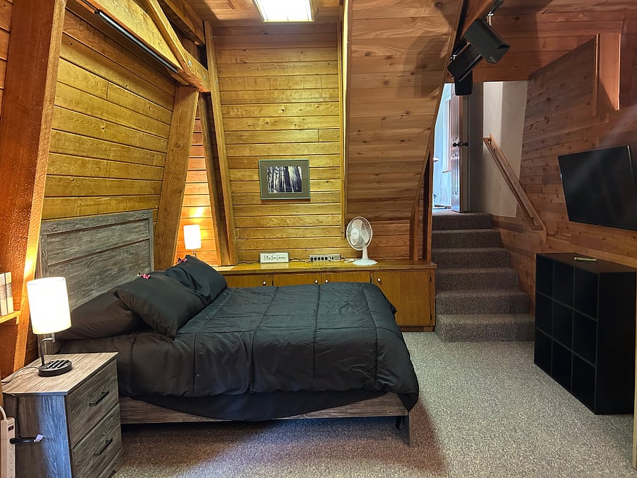 Bedroom: Queen bed and TV area, looking toward the stairs that access extra storage space
