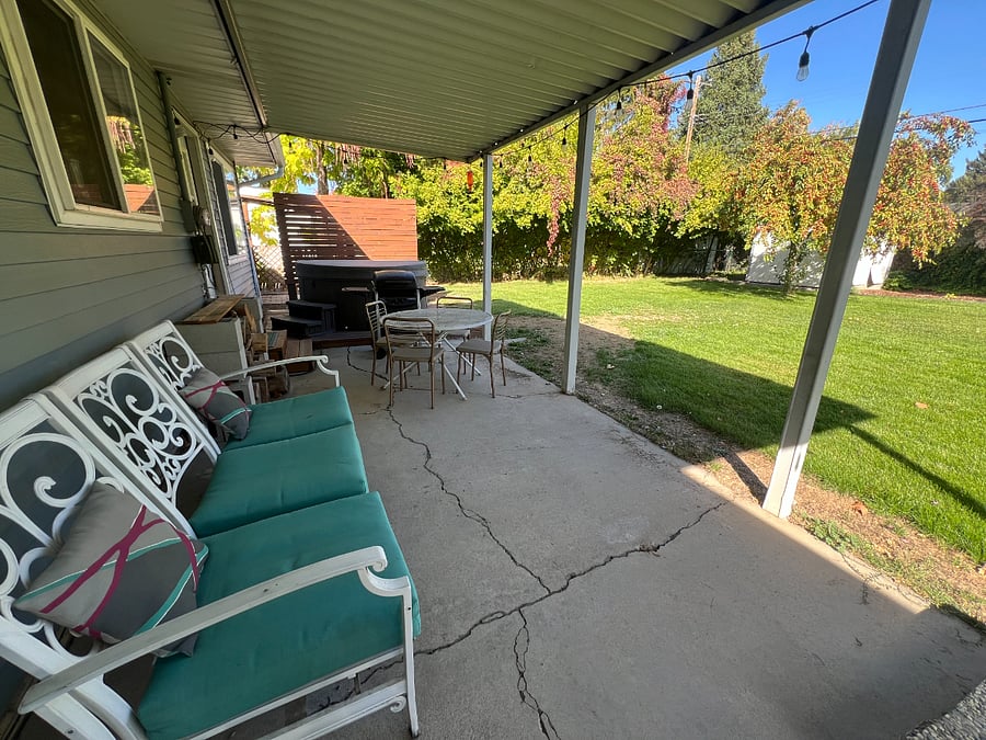 Covered patio with grill, table, and outdoor couch. Hot tub is not in working condition.