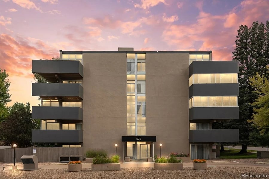 Building exterior with primary secure entrance; guest parking visible to the left and one reserved underground parking space in garage below.