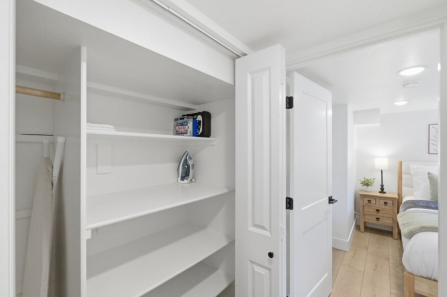 Hallway closet with storage ready shelving and full-length clothing hanging section. Iron and ironing board. 