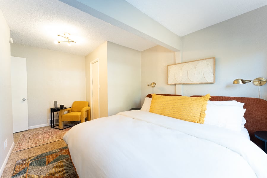 Bedroom with large window to backyard. Featuring a sitting area, walk in closet, king bed & 1/2 bath