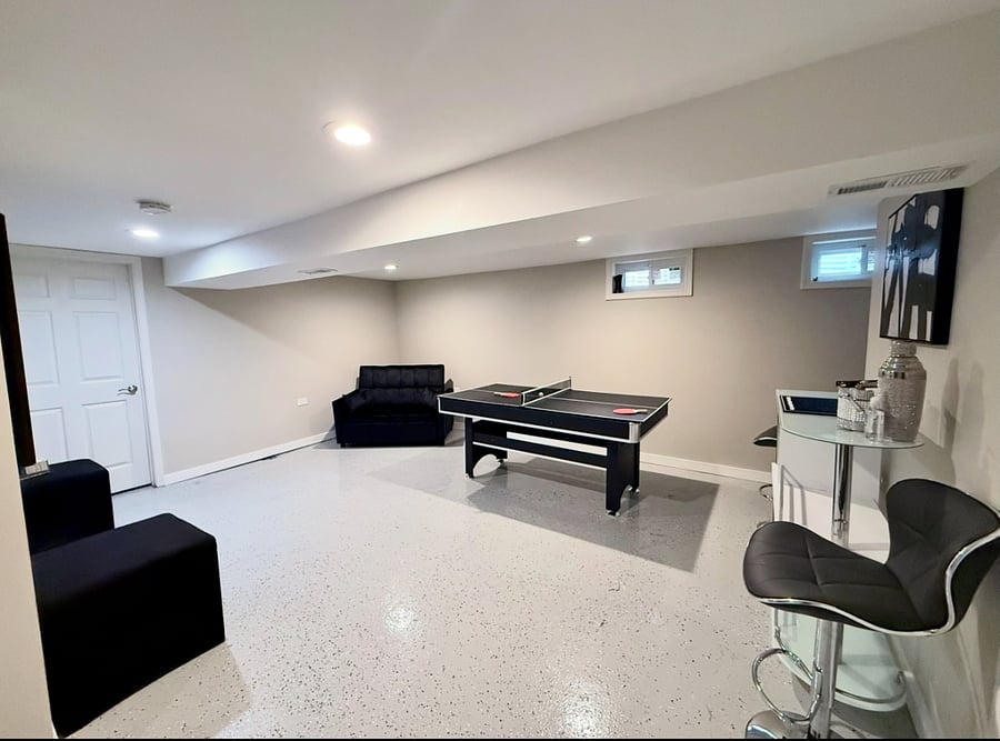 Multi-use entertainment room with 2 in 1 red felt pool/ping-pong table, large flatscreen TV and lounge area with barstool seating. Includes a couch that converts into a bed for additional sleeping space. Designed for fun, relaxation, and extra comfort.