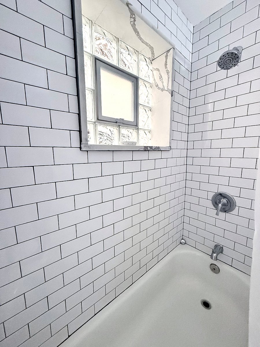 Full decorated bathroom with tub/shower combo, Toilet, And sink Vanity. Dark blue accent wall with bright lighting, And frosted glass window for privacy.