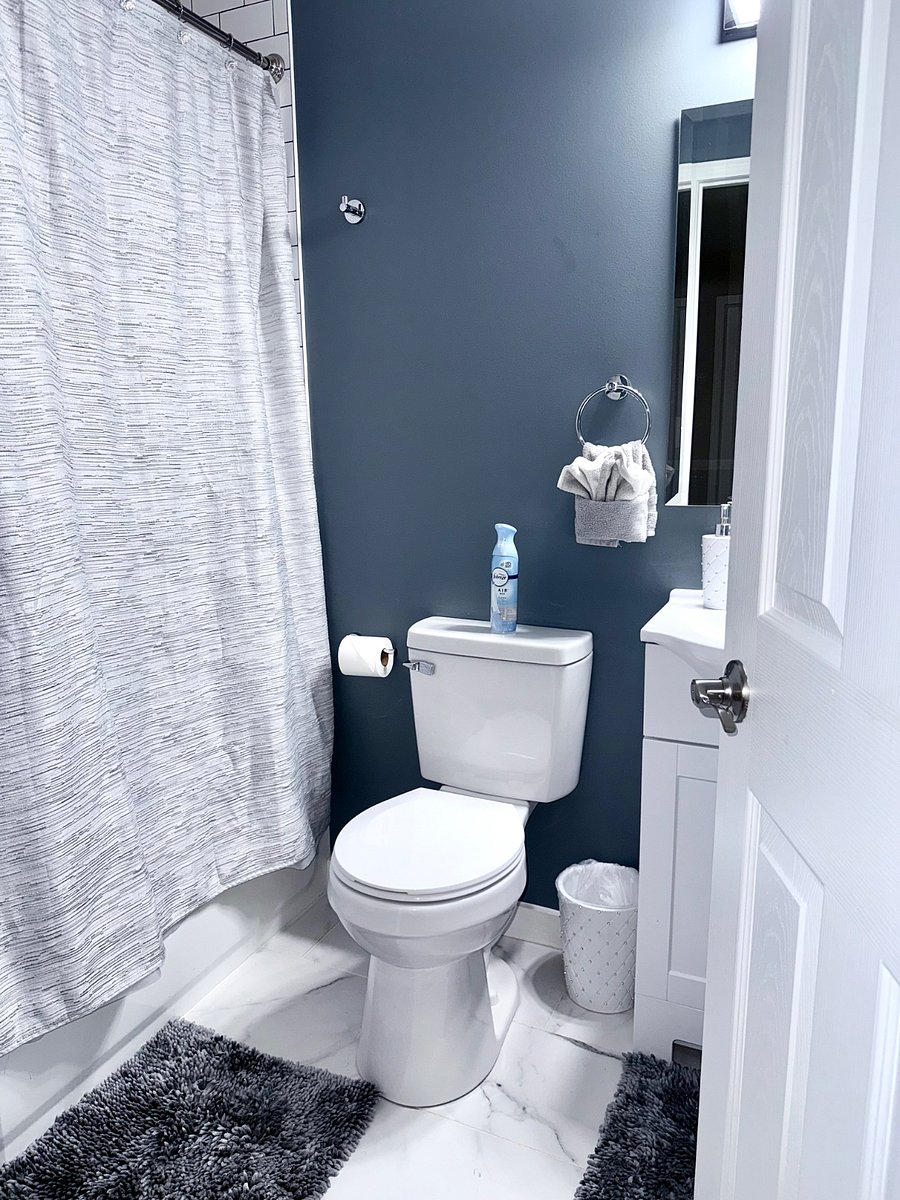 Full decorated bathroom with tub/shower combo, Toilet, And sink Vanity. Dark blue accent wall with bright lighting, And frosted glass window for privacy.