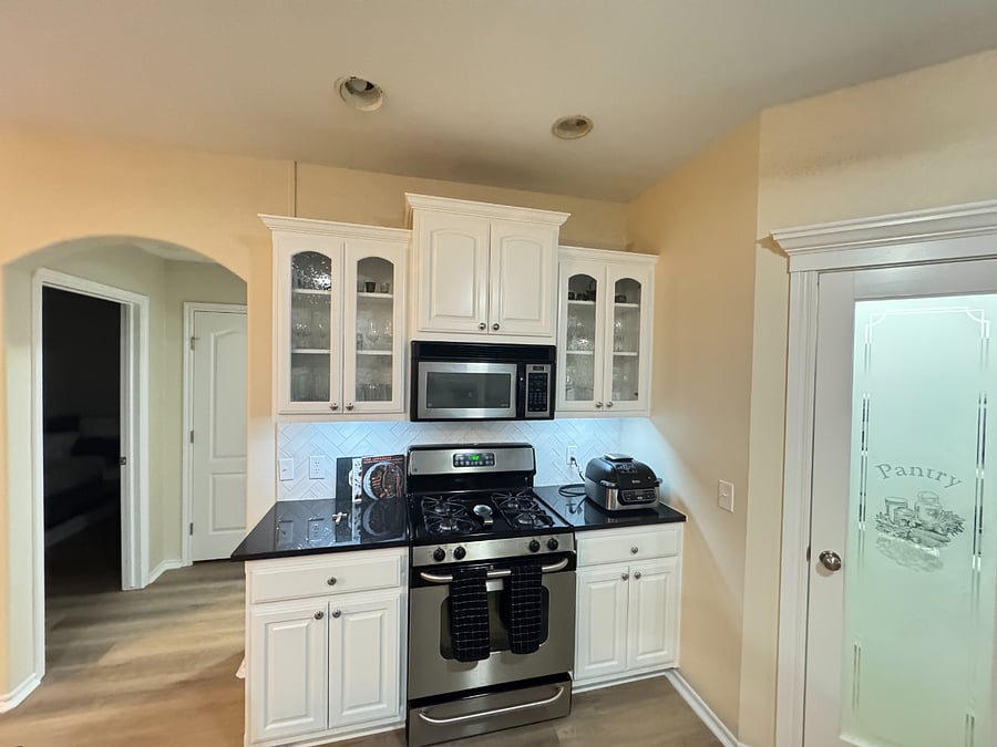 Open kitchen with black granite counters, white cabinets, and full cookware for home dining.