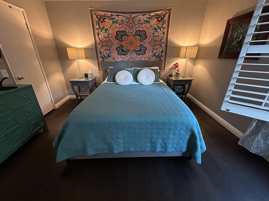 Primary/Master Bedroom. Comes with a mounted flat screen TV, a writing desk, a walk-in closet, a reading area, a double-sink vanity, and a private bathroom with a rain shower head. Window view overlooks a green flowering hill and the pool.