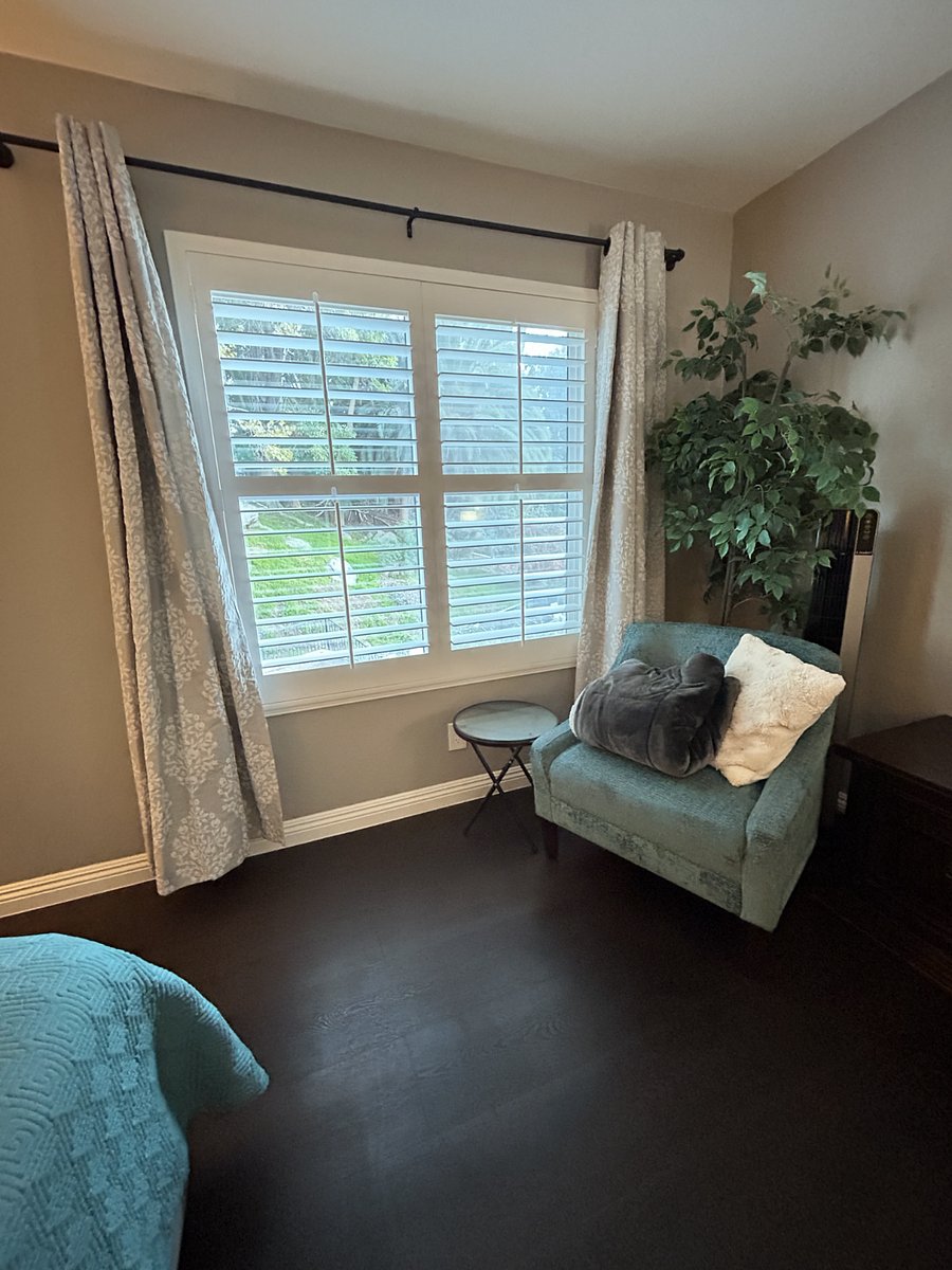Primary/Master Bedroom. Comes with a mounted flat screen TV, a writing desk, a walk-in closet, a reading area, a double-sink vanity, and a private bathroom with a rain shower head. Window view overlooks a green flowering hill and the pool.