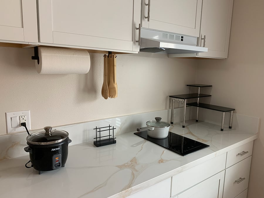 Compact, functional kitchen featuring a sleek counter-mounted stove, air fryer, rice maker, and full set of cookwareperfect for preparing home-style meals with ease and convenience during your stay.