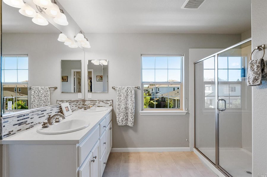 Primary bathroom with double vanity, bright lighting, and walk-in shower.