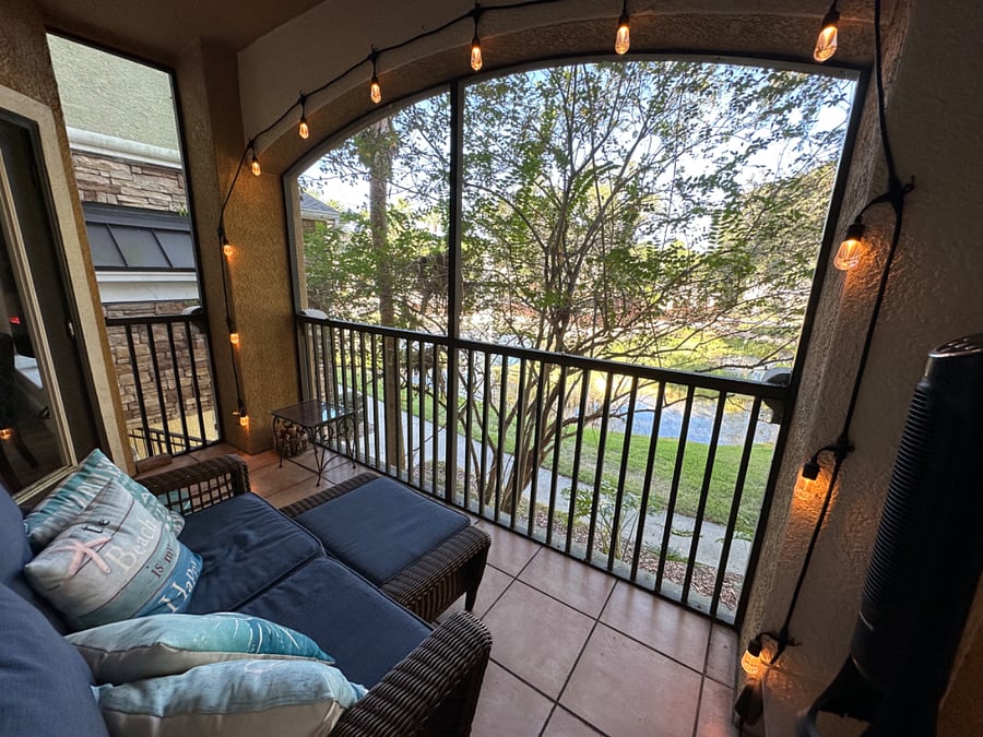 Screened porch with cozy couch and view of pond with fountain.