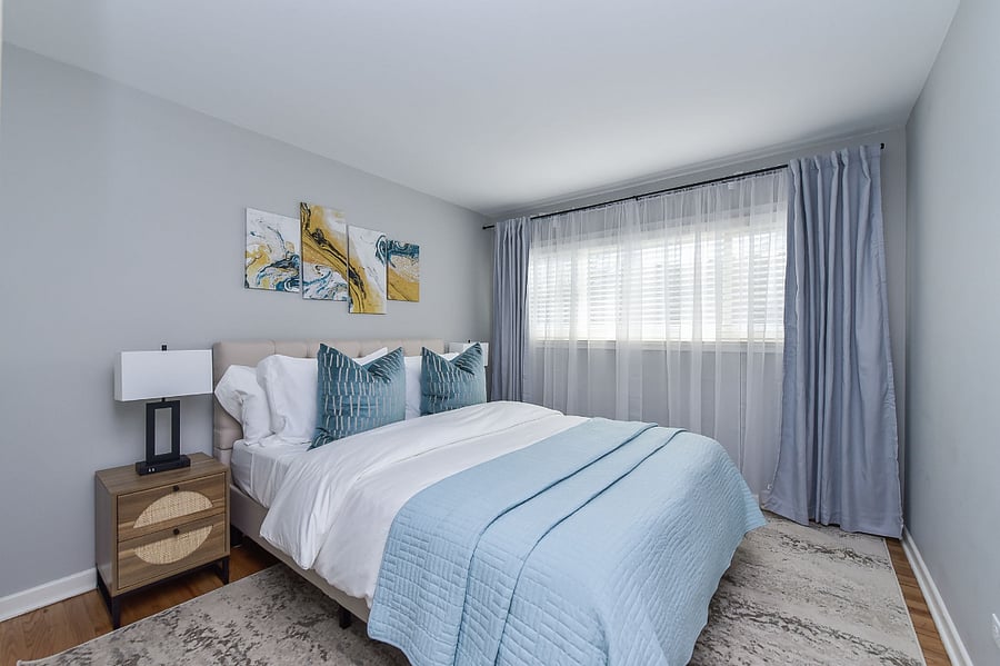 This serene bedroom is appointed with a memory foam mattress dressed in posh linens, complemented by coordinating nightstands with lamps and effective blackout blinds for a perfect night's rest.