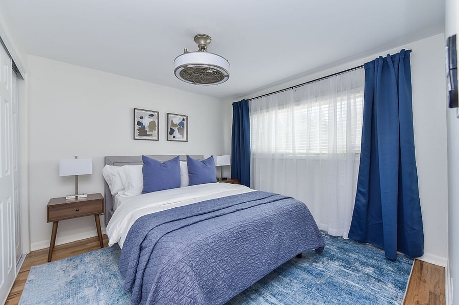 This serene bedroom is appointed with a memory foam mattress dressed in posh linens, complemented by coordinating nightstands with lamps and effective blackout blinds for a perfect night's rest.