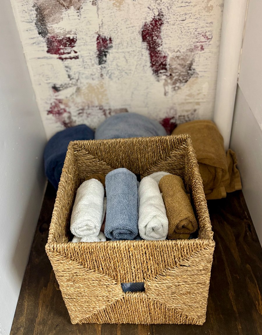 Bathroom stocked with towels, washrags, plunger, toilet cleaner, clothes hamper, and antibacterial hand soap.