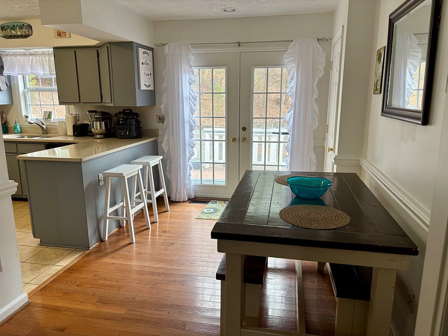 Dining room with farm house table and counter barstools. French doors lead to deck with outdoor dining and lounge seating. Interior door to the right opens to large walk-in pantry,