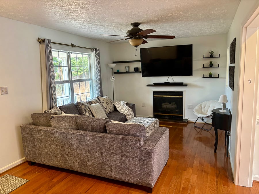 Living room with comfortable L-shaped coach and 60 inch mounted smart TV. Door leads to side porch with seating area overlooking yard.