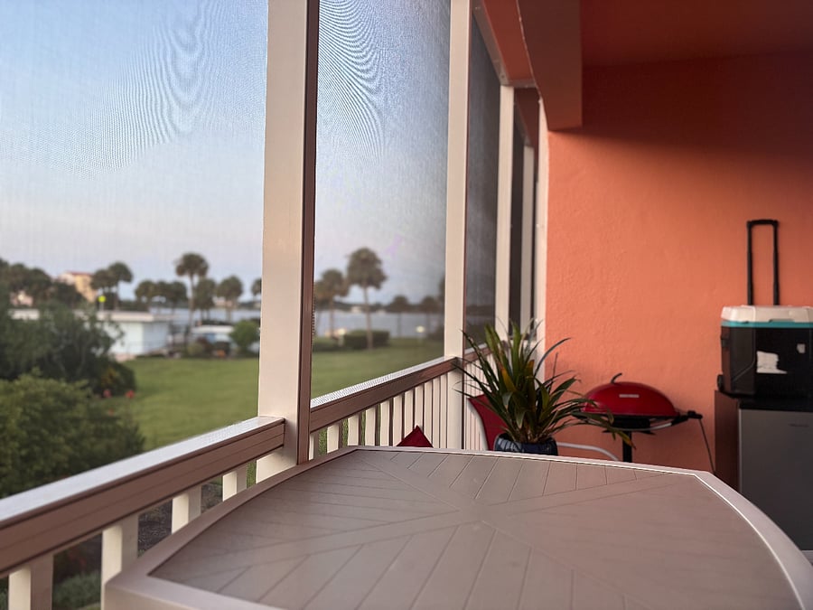 Screened in balcony off the main living space with seating for two and community approved grill
