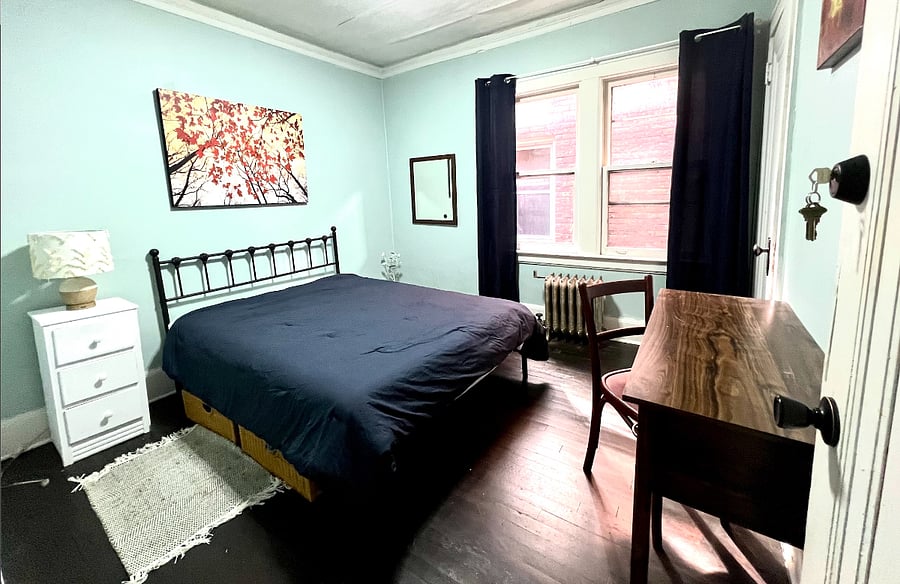 Bedroom with full size bed, desk, nightstand, lamp and under bed storage.