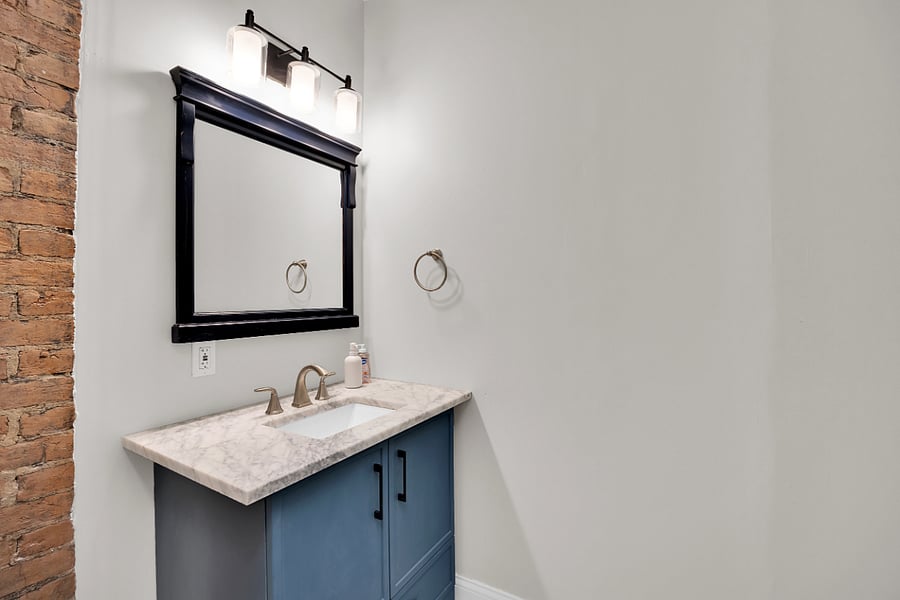 Stylish first-floor half bath featuring a modern vanity with marble countertop, updated fixtures, and exposed brick accent for added character.