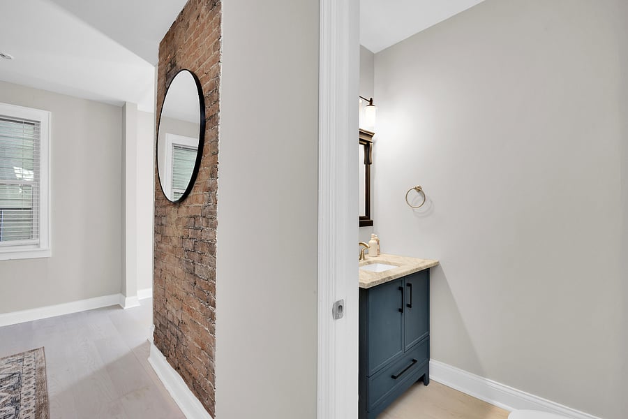 Stylish first-floor half bath featuring a modern vanity with marble countertop, updated fixtures, and exposed brick accent for added character.