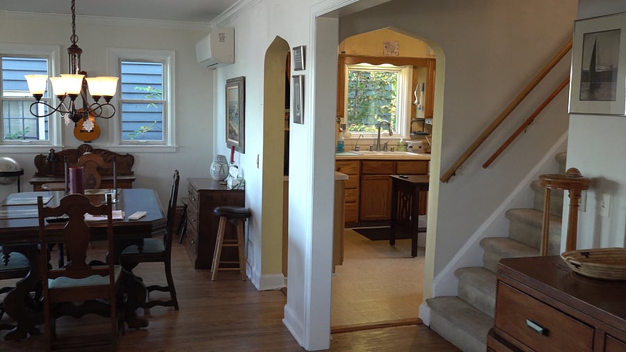 View upon entering the front door: living room is to the left, dining table is visible, kitchen entrance, and then stairs. Office is to the right.
