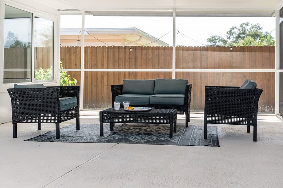 Outdoor furniture underneath a secondary roof by the pool provides screened-in relaxation.