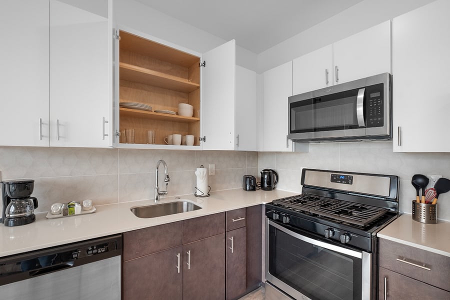 Bright, modern kitchen and living area with sleek stainless steel appliances, a stylish island with a marble countertop, and large windows that flood the space with natural light. The clean design and warm hardwood floors create a cozy yet contemporary vibe.