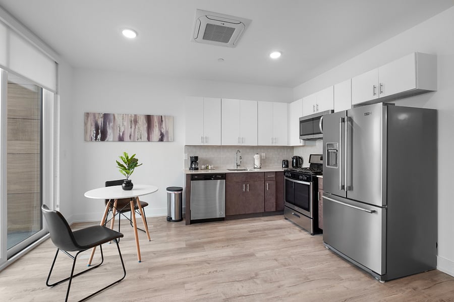 Bright, modern kitchen and living area with sleek stainless steel appliances, a stylish island with a marble countertop, and large windows that flood the space with natural light. The clean design and warm hardwood floors create a cozy yet contemporary vibe.