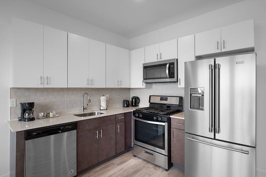 Bright, modern kitchen and living area with sleek stainless steel appliances, a stylish island with a marble countertop, and large windows that flood the space with natural light. The clean design and warm hardwood floors create a cozy yet contemporary vibe.
