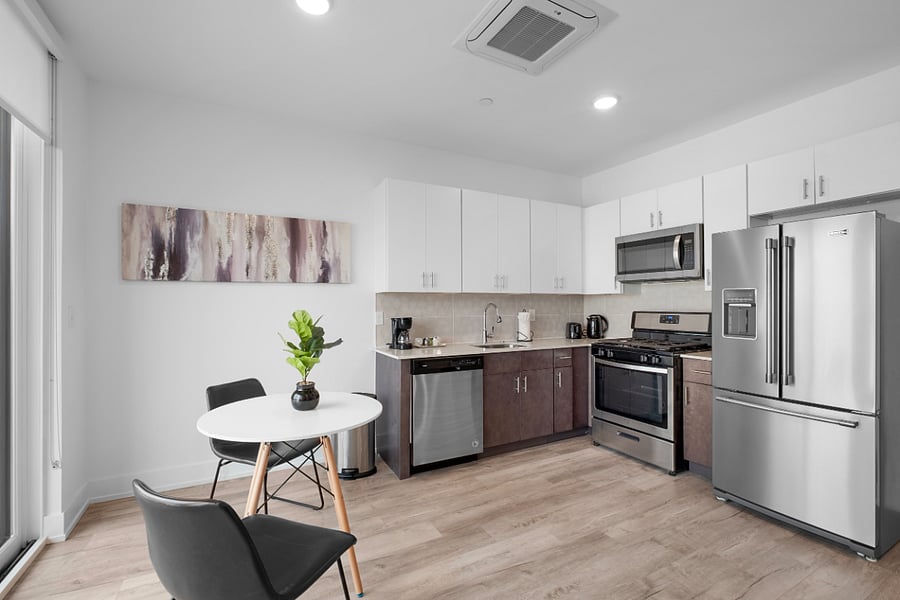 Bright, modern kitchen and living area with sleek stainless steel appliances, a stylish island with a marble countertop, and large windows that flood the space with natural light. The clean design and warm hardwood floors create a cozy yet contemporary vibe.