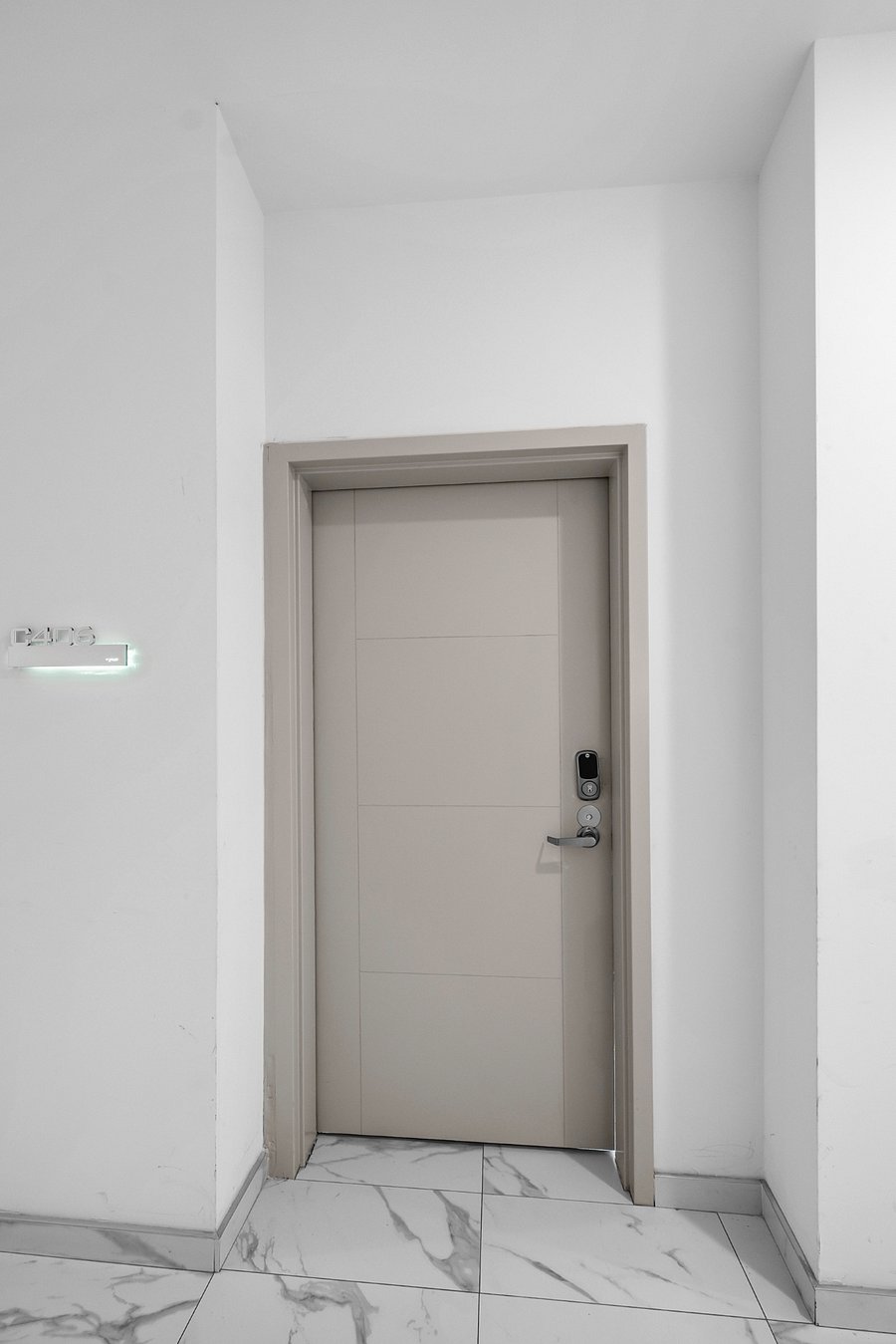 Sleek, modern white door set in a minimalist white wall. The door is equipped with a digital keypad lock and a peephole, emphasizing security and convenience.