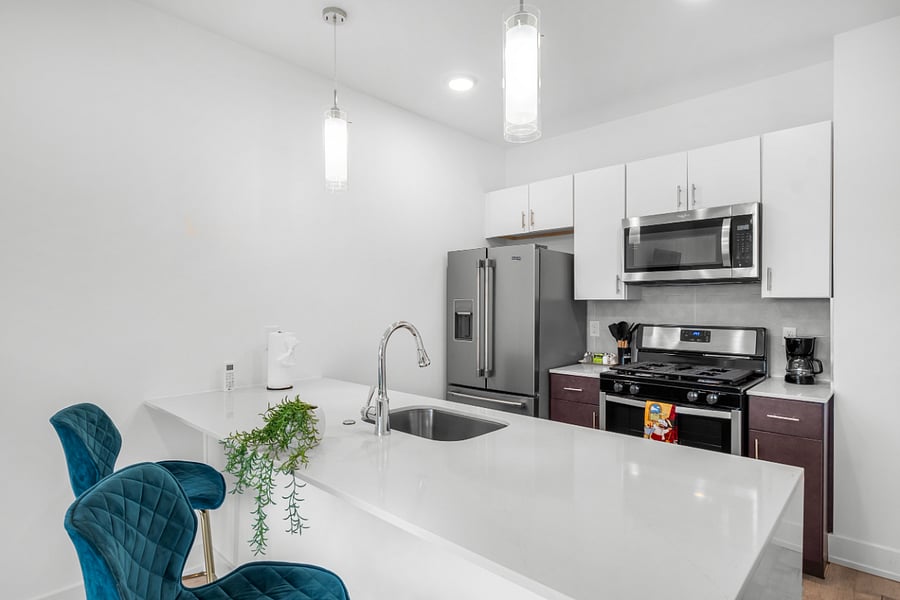 A sleek, modern kitchen with a white quartz island featuring a built-in sink and two elegant blue quilted bar stools. 