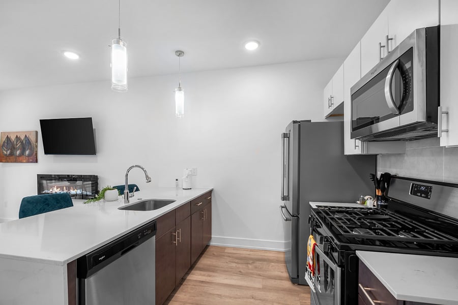 A sleek, modern kitchen with a white quartz island featuring a built-in sink and two elegant blue quilted bar stools. 