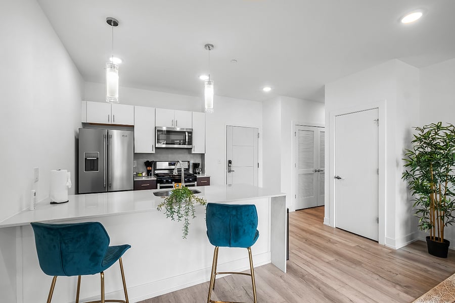A sleek, modern kitchen with a white quartz island featuring a built-in sink and two elegant blue quilted bar stools. 