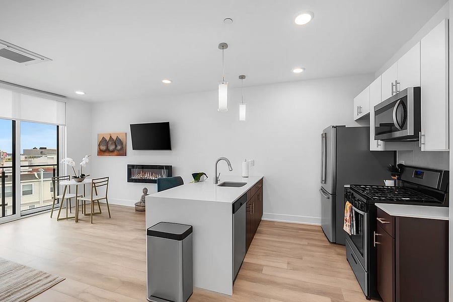 A sleek, modern kitchen with a white quartz island featuring a built-in sink and two elegant blue quilted bar stools. 