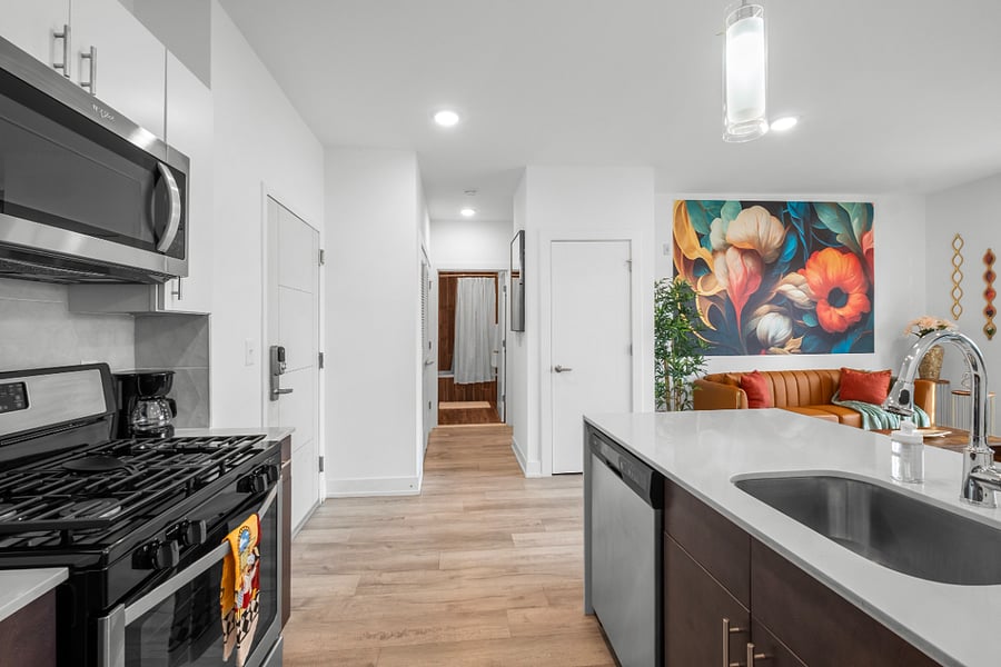 Modern open-concept kitchen and living area featuring stainless steel appliances, a dual-tone cabinet design, and a sleek island with integrated sink. 