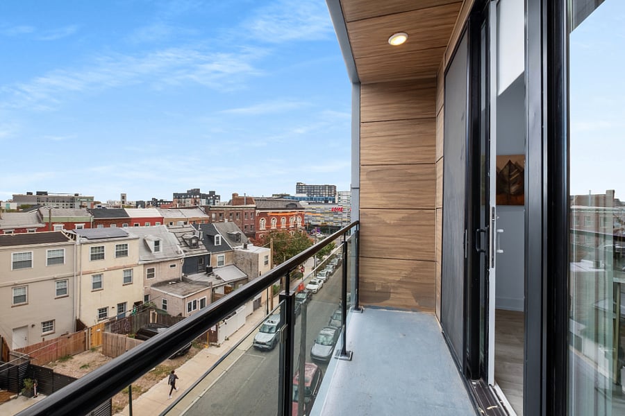 The photo captures a stylish urban apartment view from a balcony with glass railing and wood-paneled walls.