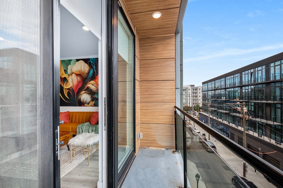 The photo captures a stylish urban apartment view from a balcony with glass railing and wood-paneled walls.