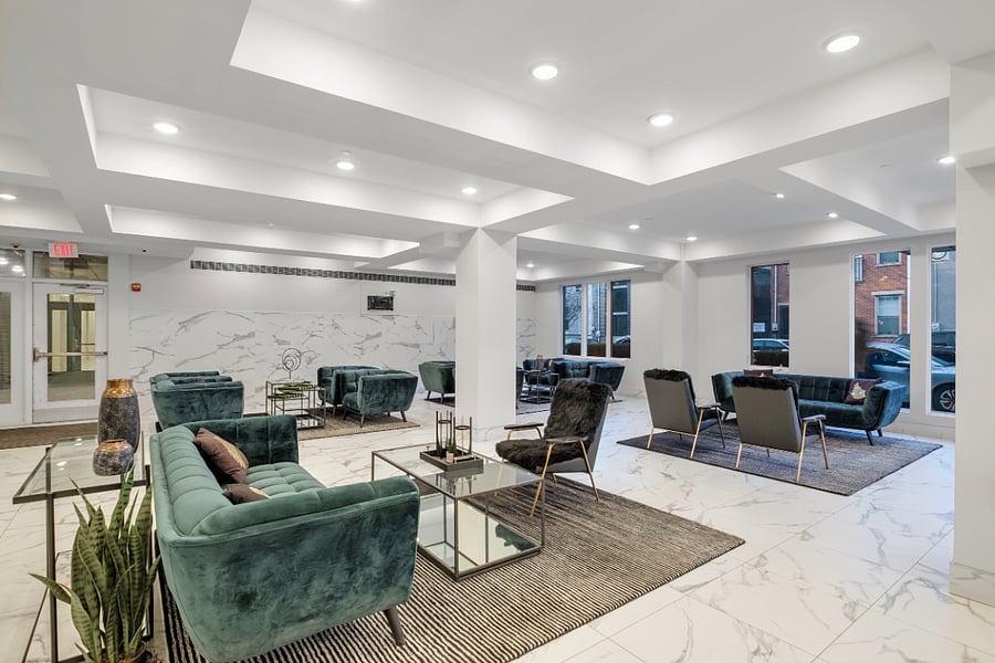 luxurious and spacious lounge area with a modern, minimalist design. Features white marble flooring with gray veining, recessed lighting in a geometric ceiling, and elegant seating arrangements