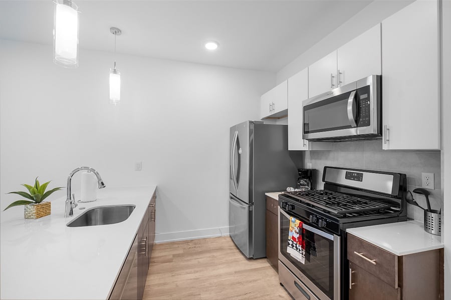 A sleek, modern kitchen with a white quartz island featuring a built-in sink and two elegant blue quilted bar stools. 