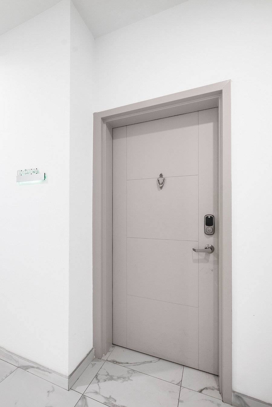 Sleek, modern white door set in a minimalist white wall. The door is equipped with a digital keypad lock and a peephole, emphasizing security and convenience.
