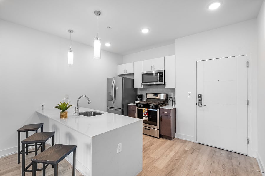A sleek, modern kitchen with a white quartz island featuring a built-in sink and two elegant blue quilted bar stools. 